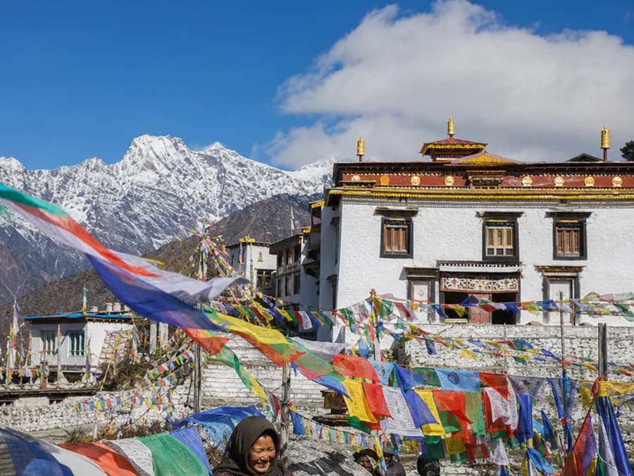 Colourful prayer flags strung before a whitewashed Buddhist monastery in the mountains under a bright sky