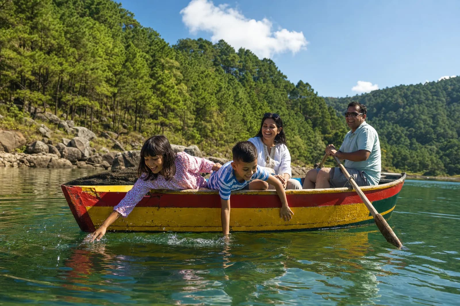A family in a small rowing boat on a bright green lake ringed with pine forest