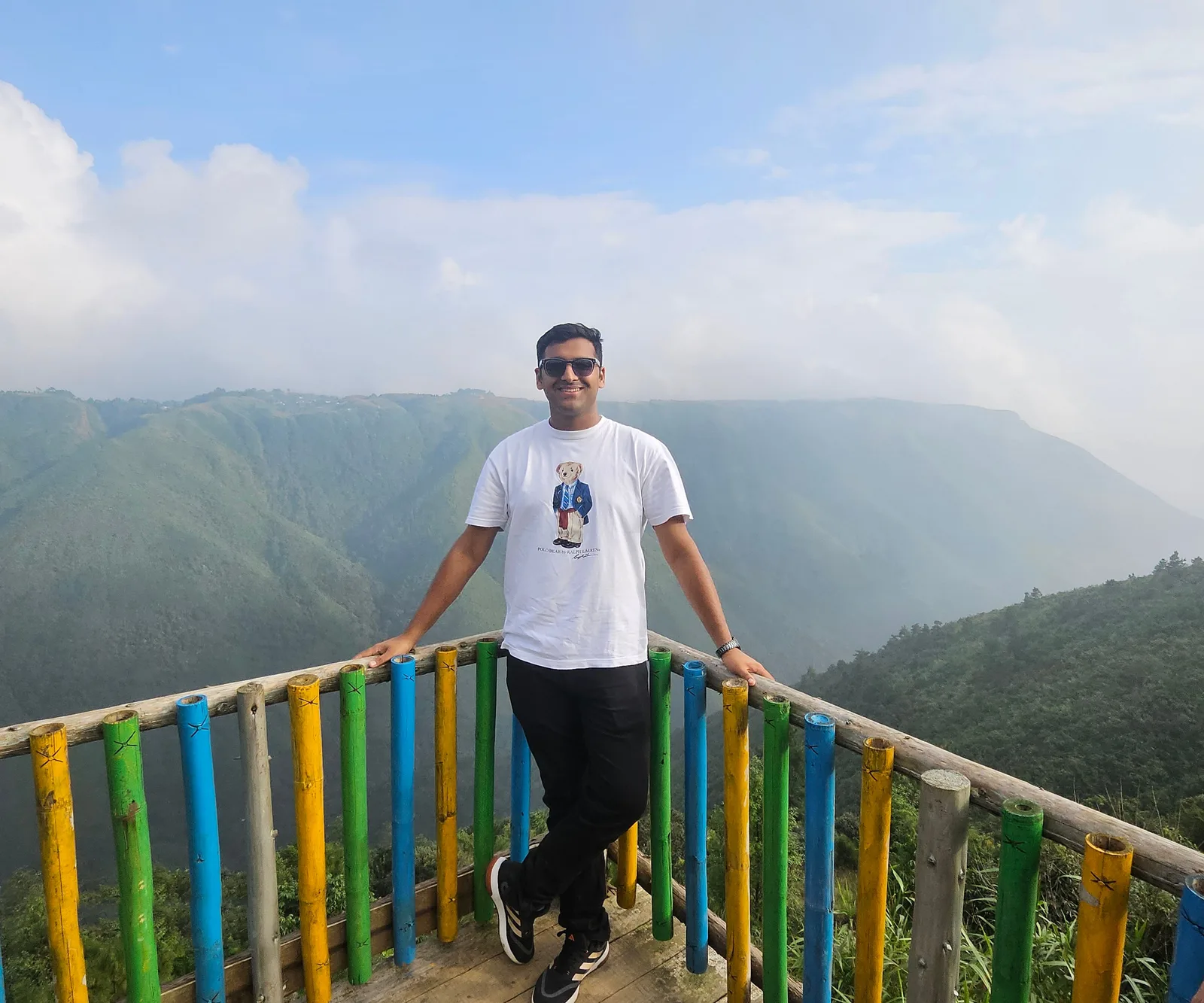 A Smarto traveller at a valley viewpoint with a painted bamboo railing in the hills of Meghalaya
